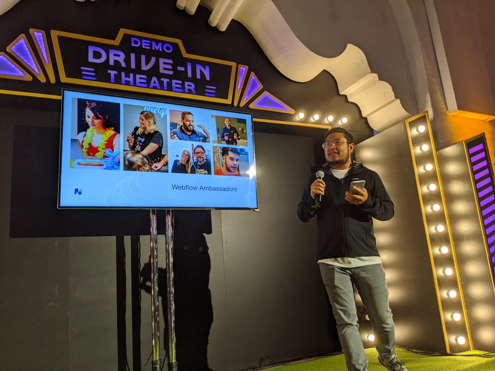 Nelson on stage with a microphone in front of a Webflow Ambassadors screen
