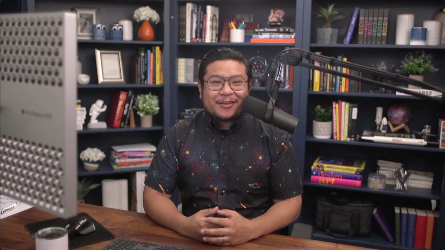 Nelson at his desk in front of a microphone and a wall of books