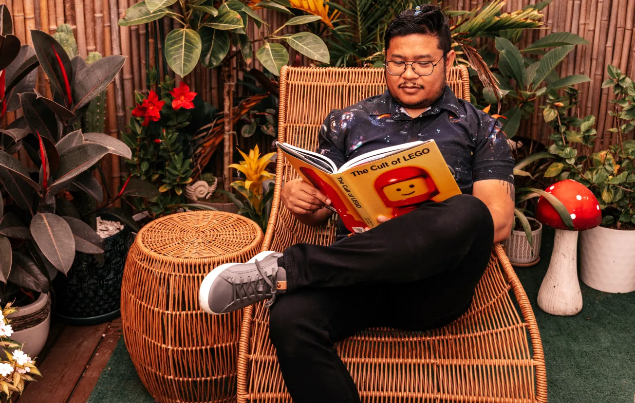 Nelson reading in a wicker chair surrounded by plants